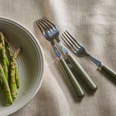 asparagus spears and forks on a white plate next to a bowl of green beans