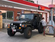 a woman is filling up her jeep at a gas station in front of a service station