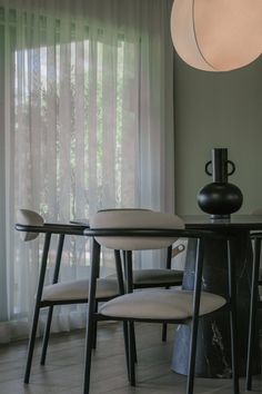 a dining room table with chairs and a vase on top of it in front of sheer curtains