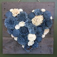 a heart made out of blue and white flowers on a wooden board with string attached to it