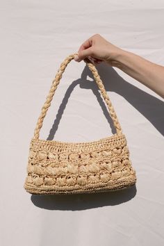 a hand holding a straw purse on top of a white table