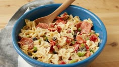 a blue bowl filled with pasta and pepperoni on top of a wooden table next to a napkin