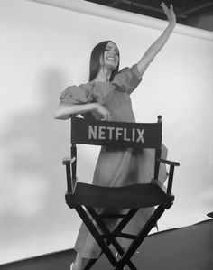 a woman sitting in a director's chair with her arms up and smiling at the camera