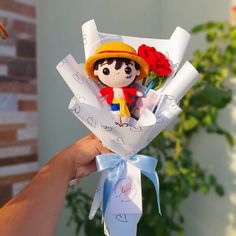 a hand holding a small doll with flowers in it's hair and wearing a hat