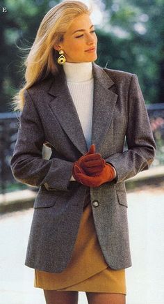 a woman wearing a gray jacket and tan skirt with her hands in her pockets while standing outside