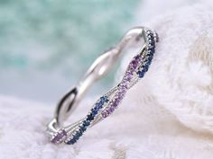 a white gold ring with purple and blue sapphires on the side, sitting on top of a pile of yarn