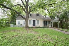 a white house sitting in the middle of a lush green yard next to a tree