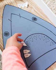 a child's hand is touching the shark shape cutout on a blue paper