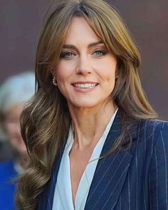 a woman with long hair wearing a blue suit and white shirt smiles at the camera