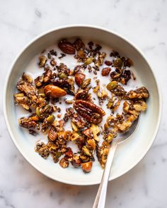 a bowl filled with granola and nuts on top of a white countertop next to a spoon