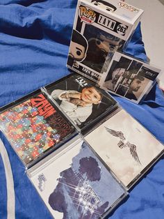 several cds are laying on a bed with blue sheets