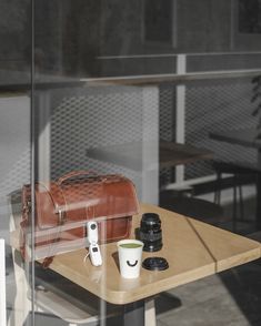 a coffee cup, camera and other items on a table in front of a glass wall