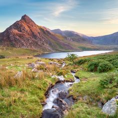 a small stream running through a lush green field next to a large mountain covered in grass