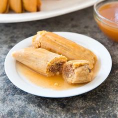 two tamales on a white plate next to a glass of orange juice