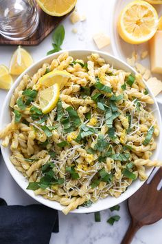 a white bowl filled with pasta and greens next to sliced lemons on a table