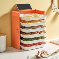 an orange and white food storage unit with six trays on each side, next to utensils