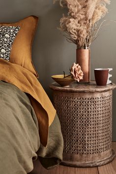 a vase with dried flowers on a table next to a bed and pillows in a room