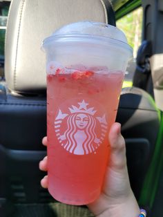 a person holding up a drink in the back seat of a car with strawberries on it