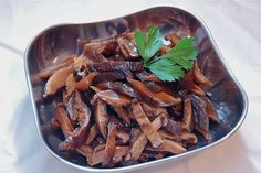 a metal bowl filled with cooked meat and garnished with green leafy parsley