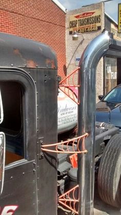 an old black truck parked in front of a brick building next to a blue car