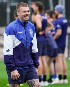 a man standing on top of a soccer field wearing a blue jacket and black shorts