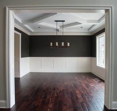 an empty living room with hard wood flooring and gray walls, white trim around the windows