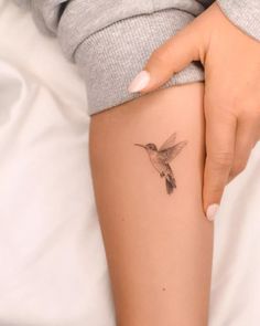 a woman's arm with a small hummingbird tattoo on the left side of her thigh