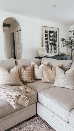 a living room with a large sectional couch and pillows on the back of it's seat