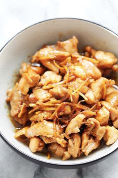 a bowl filled with chicken and sauce on top of a marble countertop next to a spoon