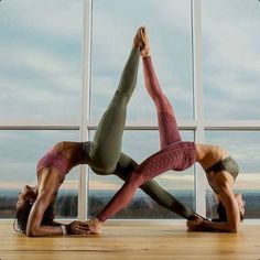 two women doing yoga poses in front of a window