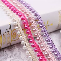 three different colored pearls and beads on a white lace table cloth with a book in the background