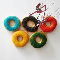 four donuts with different colored frosting and sprinkles are arranged on a white surface