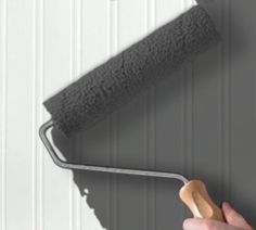 a person holding a paint roller in front of a gray wall with white paneling