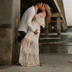 a man and woman kissing in front of the ocean under a bridge with water behind them