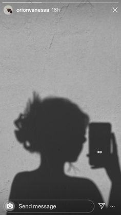 the shadow of a woman holding a cell phone up to her face, against a white wall