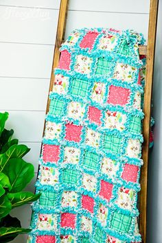 a quilted blanket sitting on top of a ladder next to a potted plant