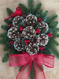 a pine cone wreath with red berries, pine cones and evergreens on it is tied to a wooden floor