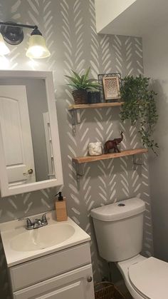 a white toilet sitting next to a sink in a bathroom under a mirror with shelves above it