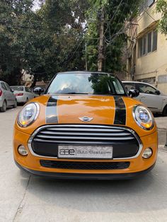 an orange and black mini car parked on the side of the road in front of some cars