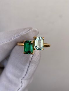 a woman's hand holding an emerald and diamond ring