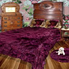 there is a bed with purple fur on it and a small white dog sitting in front of the bed