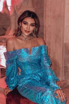 a woman in a blue dress sitting on a chair with her hand on her hip