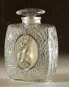 an ornate glass bottle with a dog on it's side and a small round mirror in the middle