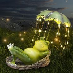 a green frog laying on top of a basket under an umbrella with lights around it