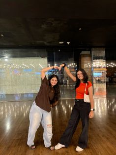 two women standing on a wooden floor holding their hands up in the air and smiling