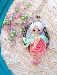 a close up of a necklace with a doll on it and pearls around the neck