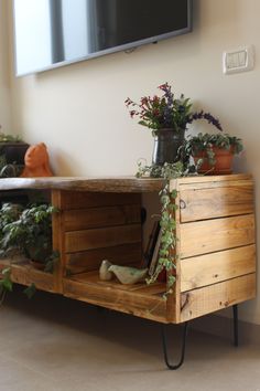 a television is mounted on the wall above a wooden cabinet with plants and books in it