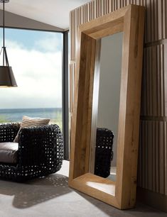 a living room with a large mirror next to a chair and window overlooking the ocean