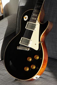 an electric guitar sitting on top of a gray couch next to a black and gold case