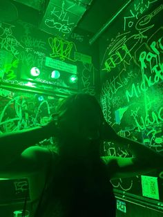 a woman standing in front of a wall covered with green and black graffiti at night